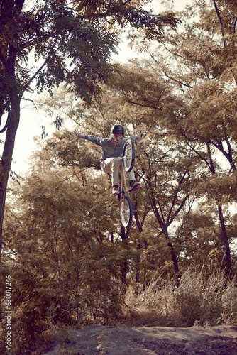 Young man, extreme sport lover riding bmx bicycle, training outdoors on hills in forest, doing tricks. High jump. Concept of active lifestyle, sport, extreme, dynamics, hobby, freestyle