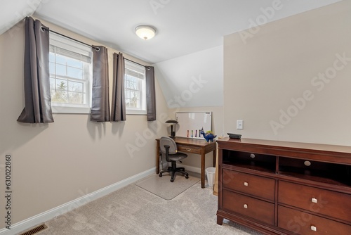 Room with two small windows  a wooden desk and a dresser.