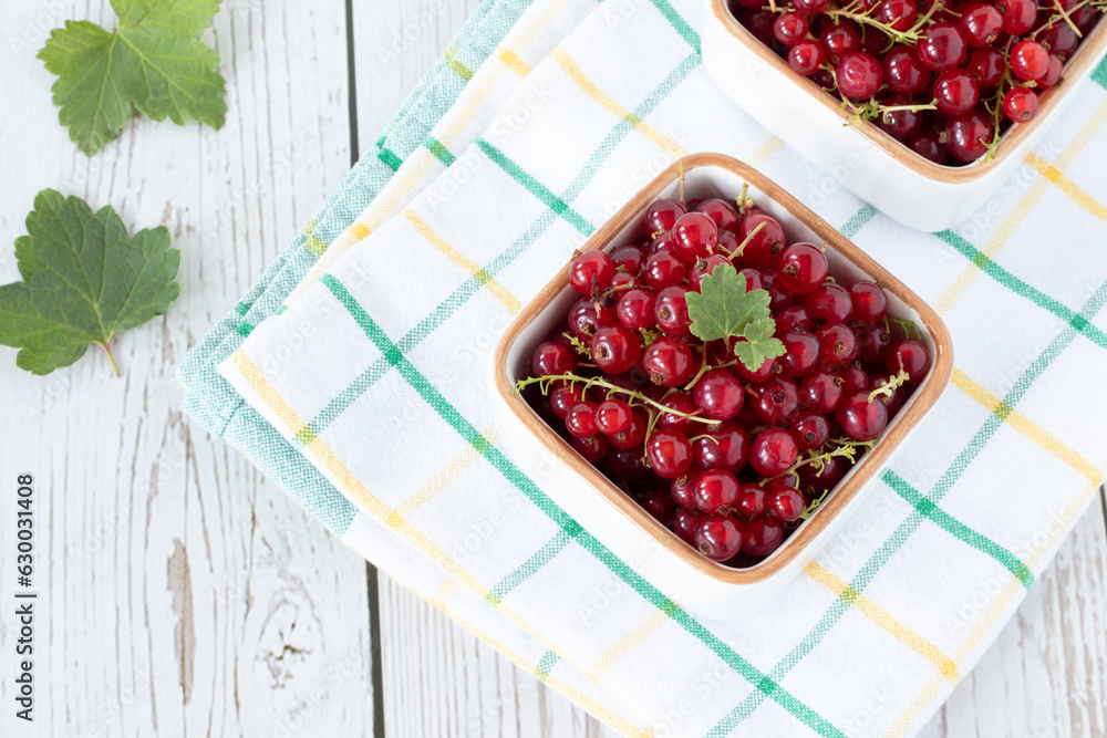 Fresh red currants with green leaves in bowls on wooden table. Top view. Eating healthy juicy summer berry fruit concept. Fresh red currants with green leaves in bowls on wooden table. Top view. Eating healthy juicy summer berry fruit concept.