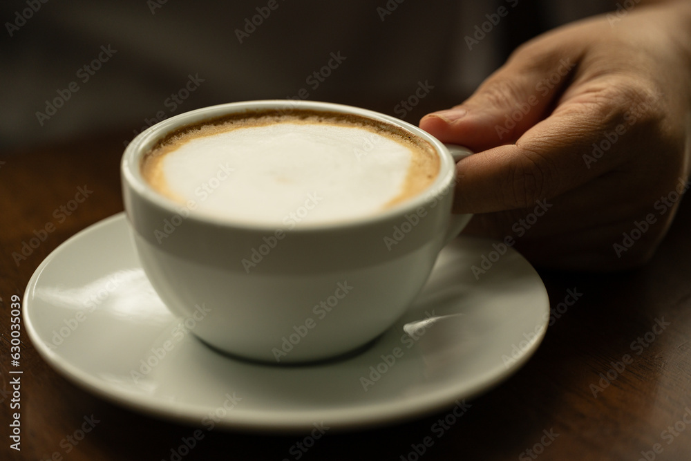 Closeup hand holding white cup of hot coffee latte on wood background in restaurant.Best of menu in the coffee shop.Soft focus.