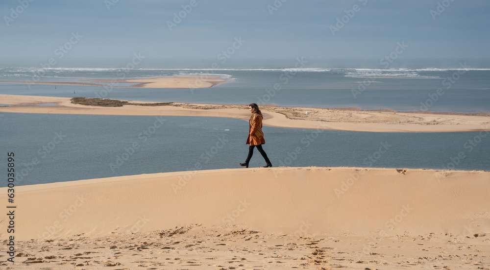 Woman walking in the French dunes in winter, wearing a coat.