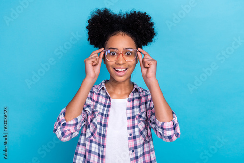 Photo of astonished speechless girl perming coiffure dressed checkered shirt touching glasses staring isolated on blue color background