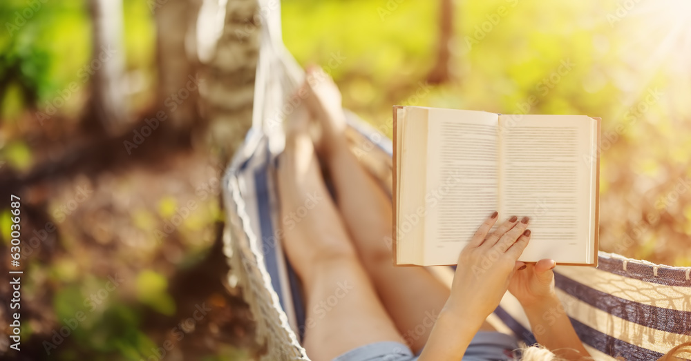 Woman lying in the hammock and reading an interesting book. - obrazy, fototapety, plakaty 