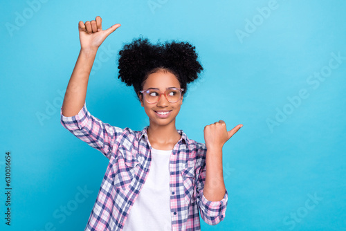 Photo of excited positive girl dressed checkered shirt eyewear pointing two thumbs empty space isolated blue color background