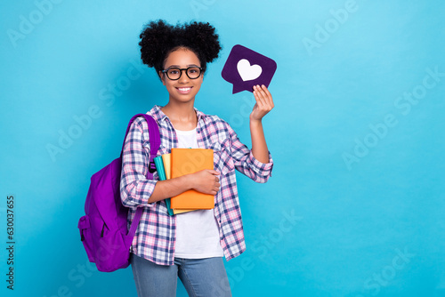 Photo of positive nice girl dressed checkered shirt backpack on shoulder holding book like icon isolated on blue color background photo