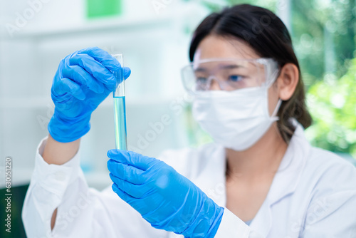 A female scientist is holding a blue chemical substance in laboratory. Concept of checking the quality of sample liquid or biotechnology and medicine research, examining, inspection or discovery.