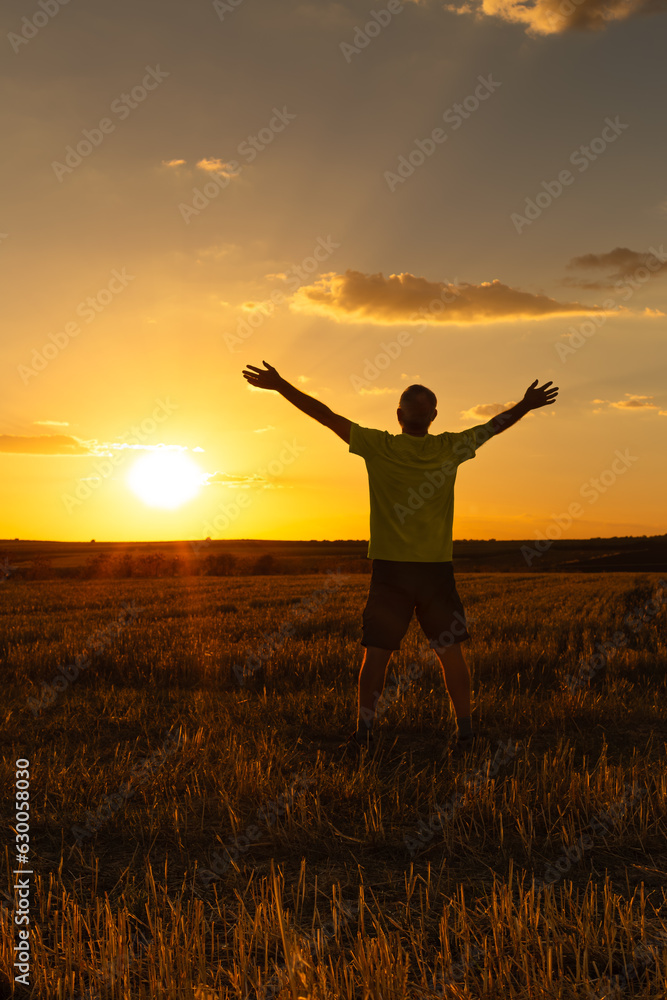 A man on his back with his arms open and outstretched in the middle of the field is watching and enjoying the sunset in the summer day. Vertical.