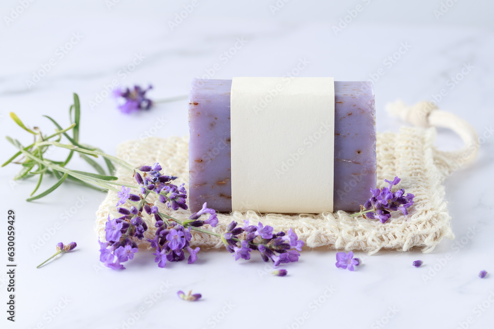 Aroma herbal handcraft soap with lavender flowers for bath relaxation and body care on sisal net bag over white marble table background. Home spa lifestyle. - obrazy, fototapety, plakaty 