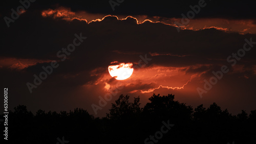 Landscape with red sun setting behind dark clouds