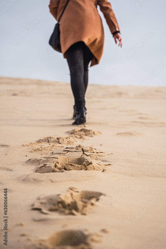 footprints in the sand, in black boots and brown coat, walking in the dunes.