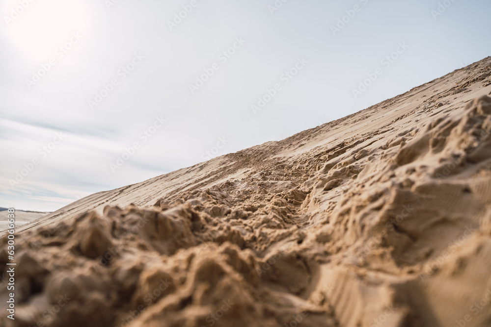 footprints in the sand, in black boots and brown coat, walking in the dunes.