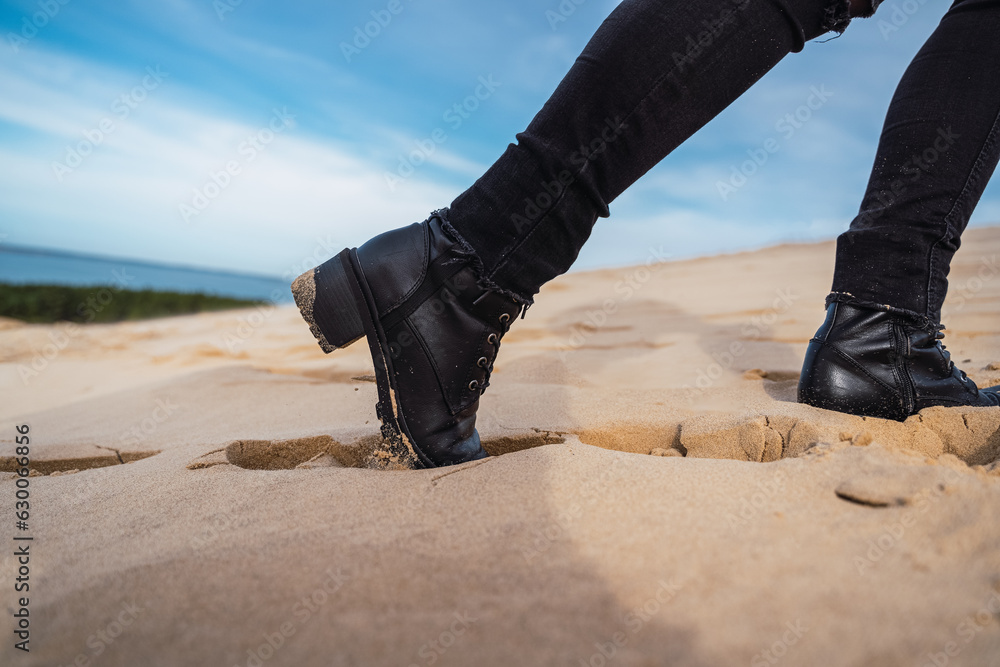 footprints in the sand, in black boots and brown coat, walking in the dunes.