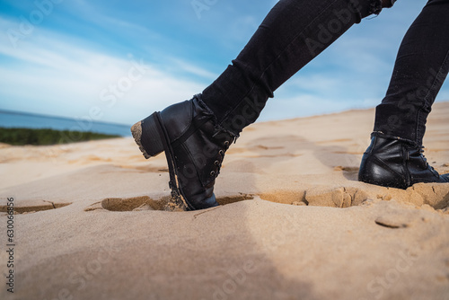 footprints in the sand, in black boots and brown coat, walking in the dunes.