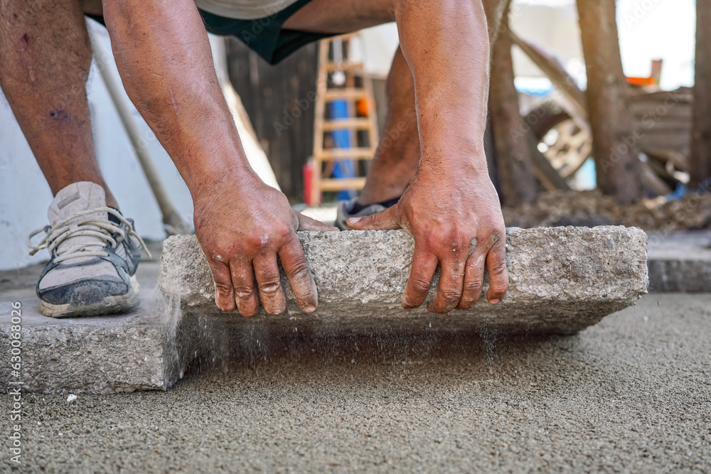 Installing new pavement or floor outside from large concrete tiles, closeup detail on male worker fitting stone block over sand and gravel base layer Installing new pavement or floor outside from large concrete tiles, closeup detail on male worker fitting stone block over sand and gravel base layer