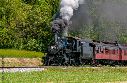 A View of an Antique Restored Steam Passenger Train, Approaching, Blowing Black Smoke, Traveling Thru Rural Countryside on a Sunny Day