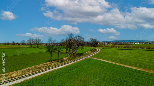 A Drone View of a Single Rail Road Track, Going Around a Curve, Thru Green Farmlands on a Blue Sky, With Clouds Day