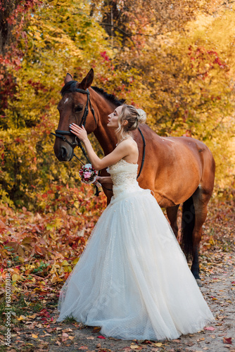Young bride hugging a horse in the autumn forest. Wedding in nature in autumn