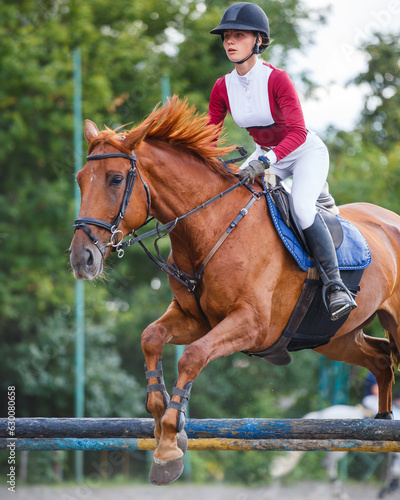 Young woman riding horseback jumping over the hurdle on showjumping course