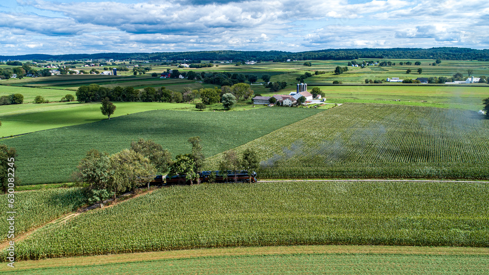 A Drone View of a Streamlined Steam Locomotive Traveling Thru Corn Green Fields, Blowing Lots of Smoke on a Sunny Summer Day