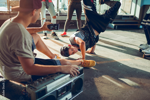 Group of young people break dancing in a parking lot and recording with their smart phone © Geber86