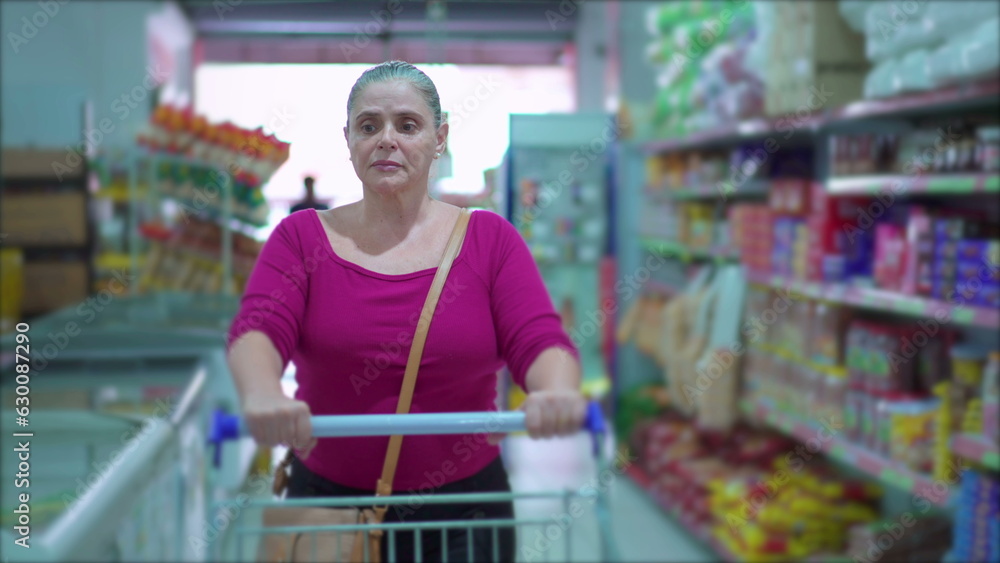 Middle-Aged Woman Shopping in Supermarket walking through aisle browsing products on shelf, Display of Consumerism