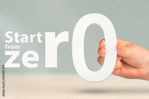 Start from zero. Close-up concept photo of a hand holding a white zero. Motivational text with a call to start everything from scratch or from the beginning. High quality photo