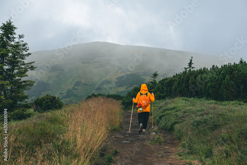 woman in yellow raincoat at mountain trail road