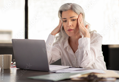 Unhappy Middle Aged Businesswoman Having Stress And Headache At Workplace photo
