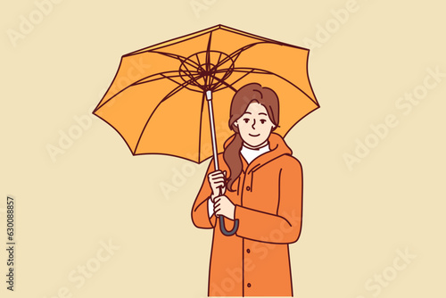 Woman with umbrella is dressed in oilcloth coat so as not to get wet from rain on autumn walk. Happy girl holding umbrella and looking at screen offering to take walk during rainy weather