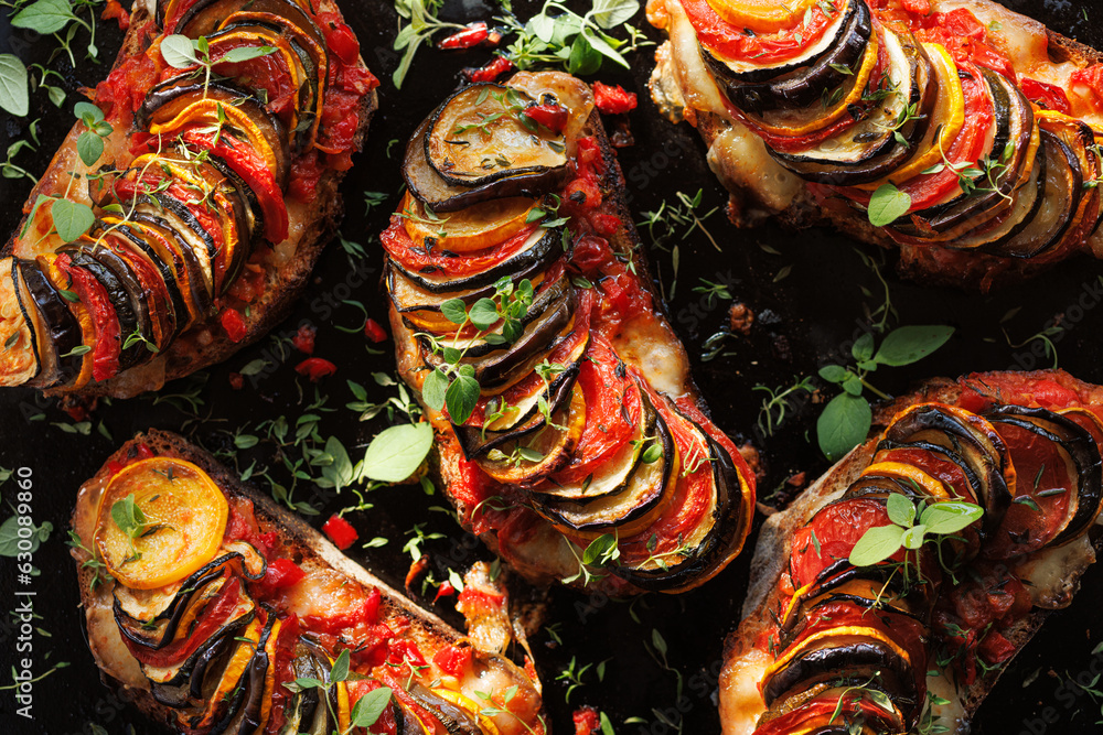 Naklejka premium Grilled sourdough bread open faced sandwich with sliced vegetables and mozzarella cheese sprinkled with fresh herbs on a black background, top view. Tian sandwich