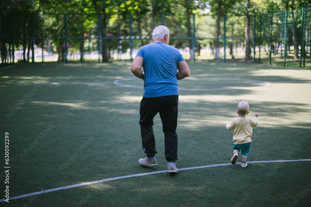 Obraz premium a gray-haired senior man 50 years old runs with his grandson in a race in the park on the sports ground
