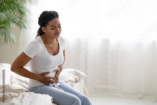 Black woman suffering stomach pain, sitting on bed and touching belly Free Download Black woman suffering stomach pain, sitting on bed and touching belly - GFXLoad