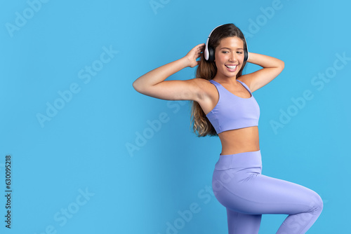 Fototapeta Naklejka Na Ścianę i Meble -  Glad young caucasian woman in sportswear and wireless headphones listens to music, dance
