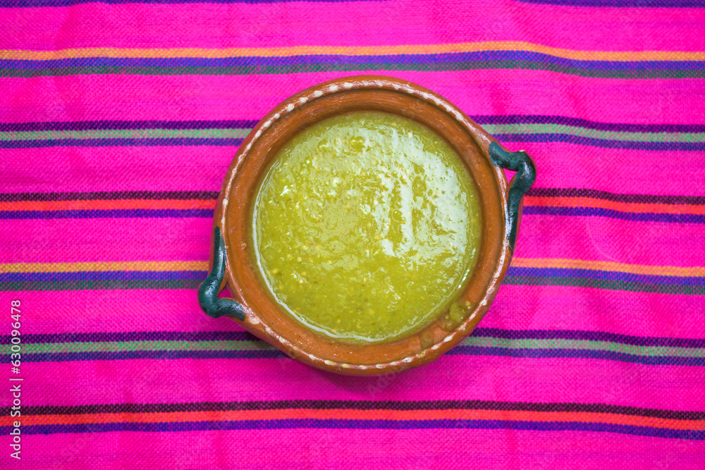 Mexican green sauce in a clay plate on a colorful tablecloth. mexican food concept Mexican green sauce in a clay plate on a colorful tablecloth. mexican food concept