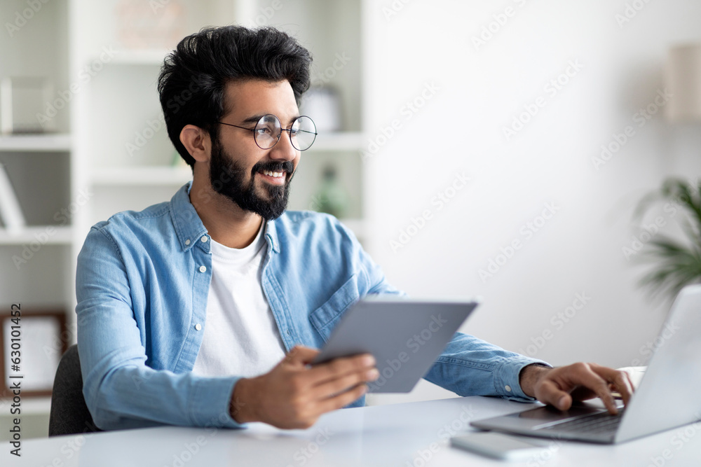 Handsome Young Indian Man Working With Digital Tablet And Laptop At Desk Handsome Young Indian Man Working With Digital Tablet And Laptop At Desk