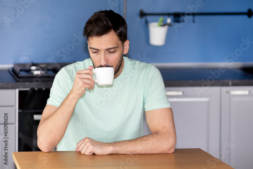 Thoughtful man sitting at the table in the kitchen and drinking hot coffee