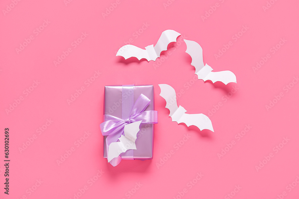Composition with beautiful gift box and bats made of paper for Halloween on pink background Composition with beautiful gift box and bats made of paper for Halloween on pink background