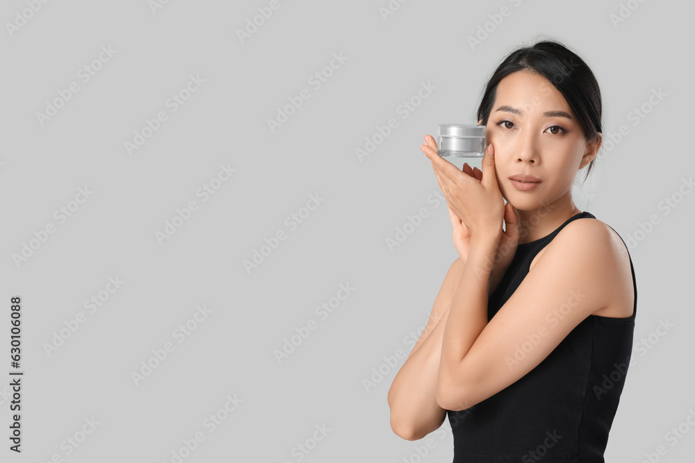 Beautiful young Asian woman with cream on grey background Beautiful young Asian woman with cream on grey background