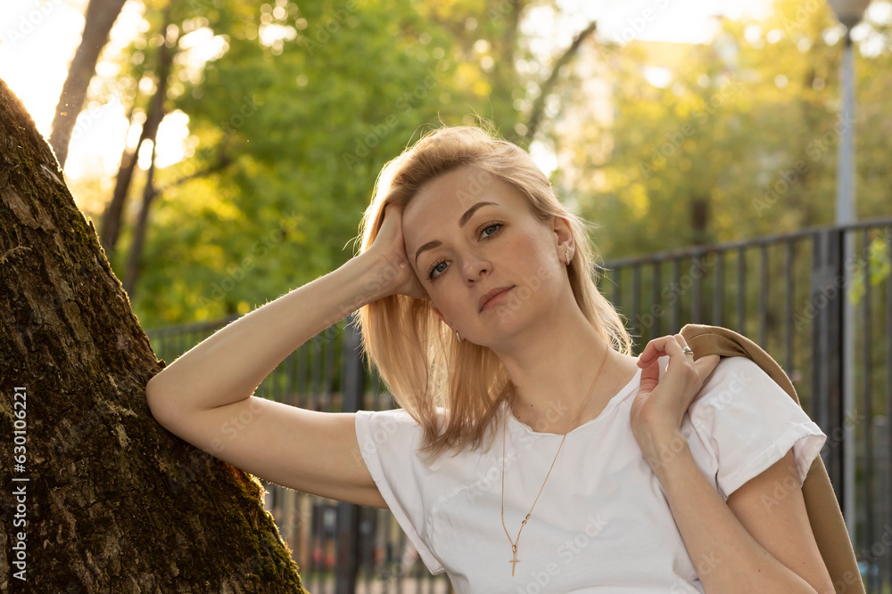 Tired Caucasian Real Woman Leans To Tree, Looks At Camera In Summer Time on Sunset. Rest And Recharge in Nature, Self Awareness, Leisure Time, Mental Health. Lifestyle Beautiful Female Horizontal 