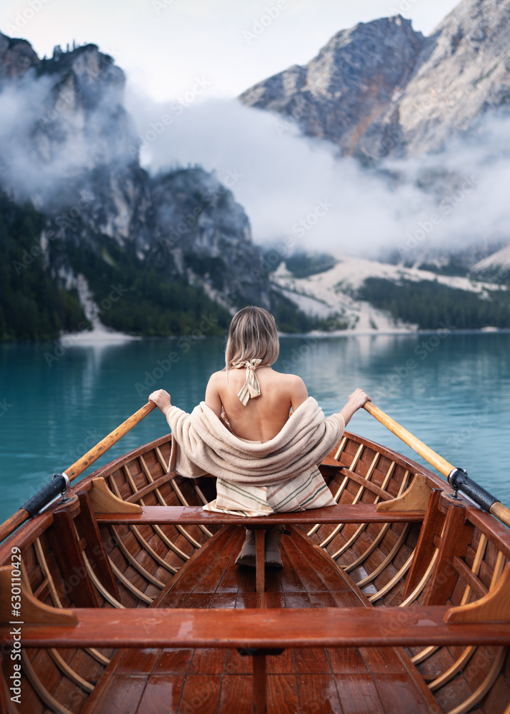 Beautiful girl sitting backwards on a boat and holding oars on the famous blue lake. Stunning romantic place with typical wooden boats on the alpine lake,(Lago di Braies) Braies lake,Dolomites