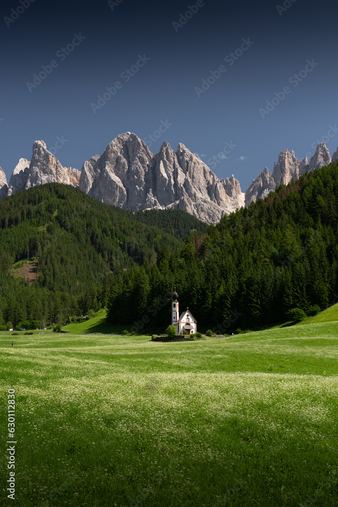 A beautiful old church among a green meadow with mountain peaks in the background. st. John church in Italian dolomites
