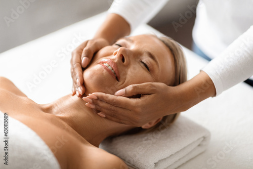 Portrait of relaxed middle aged woman having facial massage in spa center