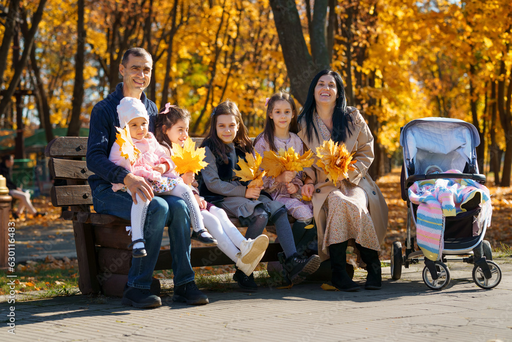 portrait of big family with children in an autumn city park, happy people sitting together on a wooden bench, posing and smiling, beautiful nature, bright sunny day and yellow leaves