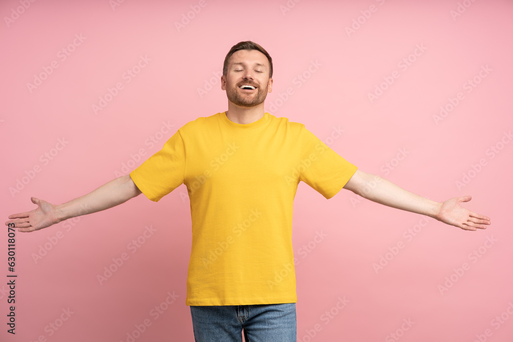 Portrait of happy young man spreading arms wide wanting to hug you with closed eyes. Friendly carefree male in yellow t-shirt stand on studio pink background. Cuddling, hugging, sincere human emotion. Portrait of happy young man spreading arms wide wanting to hug you with closed eyes. Friendly carefree male in yellow t-shirt stand on studio pink background. Cuddling, hugging, sincere human emotion.