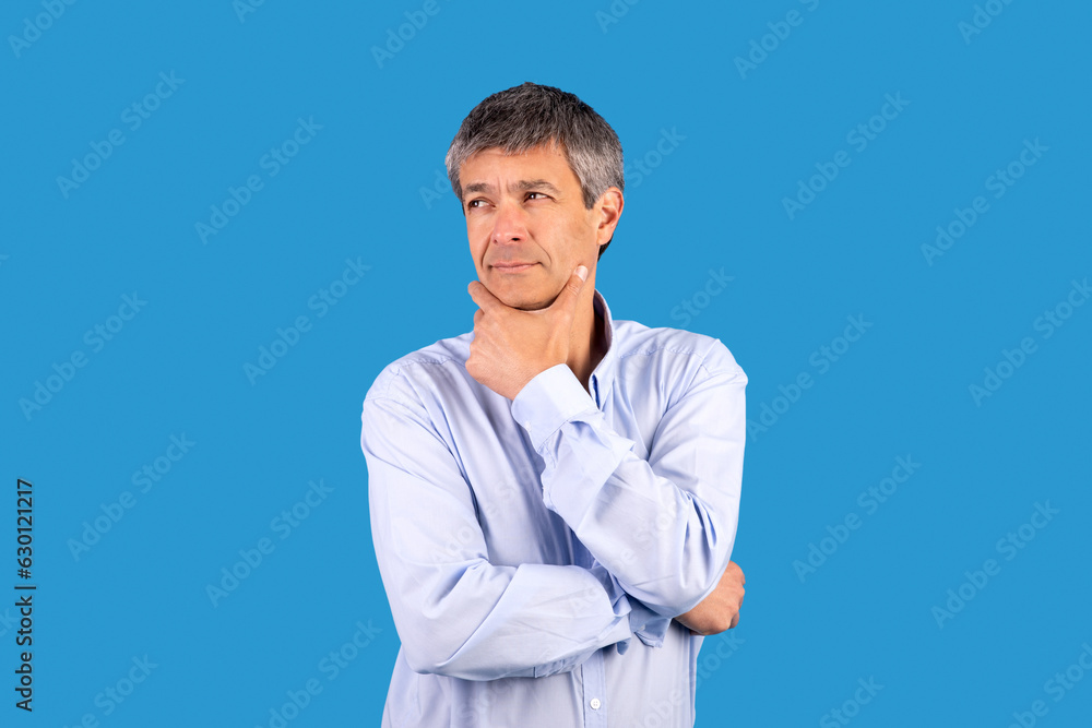 Pensive mature man touching chin with thoughtful expression, blue background Pensive mature man touching chin with thoughtful expression, blue background