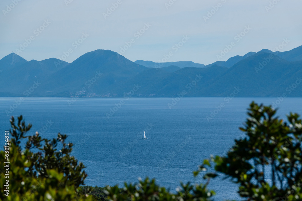 Beautiful view of a distant sailboat sailing peacefully on the blue Adriatic Sea