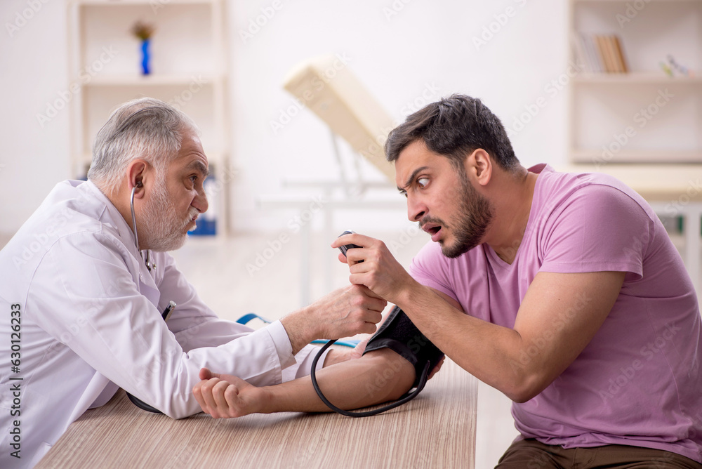 Fototapeta premium Old male doctor measuring young patient's blood pressure