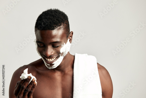 Fototapeta Studio portrait of handsome black guy with naked torso applying cream on his face
