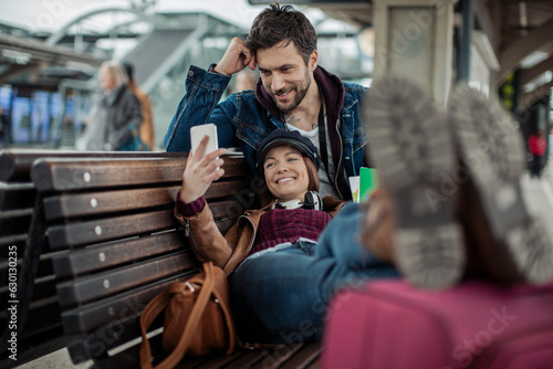 Young couple using a smart phone while waiting for their train at a train station while traveling
