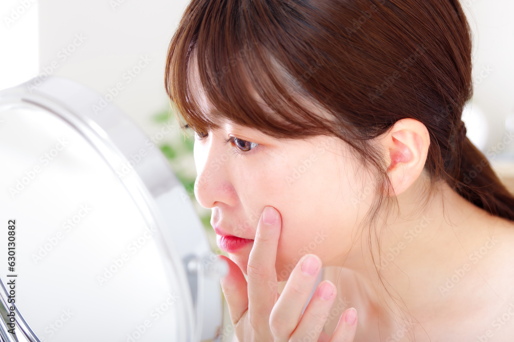鏡を見ながら顔のスキンケアをする若い女性